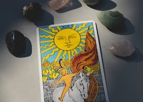 pexels-photo-7947792-7947792 A tarot card titled 'The Sun' surrounded by various healing crystals, illuminated by sunlight.